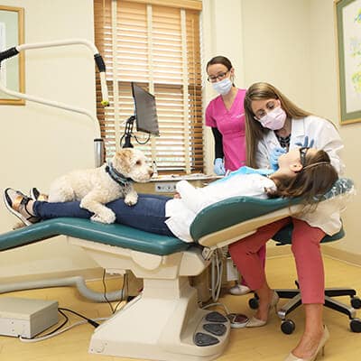Dr. Griffin checking the mouth of a girl in the dental office while a puppy sits on the patient's lap